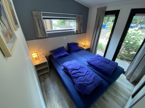 Modern bedroom with double bed, blue bedding, large windows at Pavilion 6, De Utrechtse Heuvelrug, Netherlands.