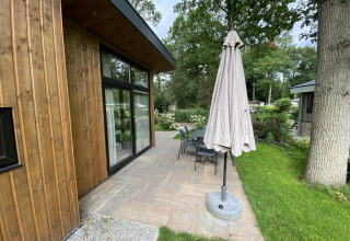 Outdoor patio of Pavilion 6 at De Utrechtse Heuvelrug, Netherlands, with wooden lodge, table, chairs, and umbrella.