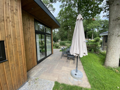 Outdoor patio of Pavilion 6 at De Utrechtse Heuvelrug, Netherlands, with wooden lodge, table, chairs, and umbrella.