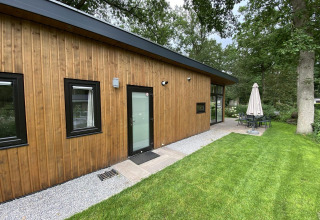 Modern wood-clad lodge Pavilion 6 at De Utrechtse Heuvelrug in the Netherlands with patio and lush garden area.