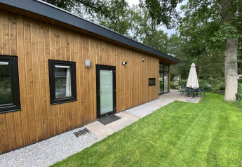 Moderne træhytte Pavilion 6 ved De Utrechtse Heuvelrug, Holland med terrasse og grøn have omgivet af træer.