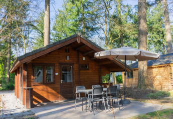 Foto del lodge Stuga 4, una confortevole baita in legno con patio, tavolo, sedie e ombrellone nel bosco.