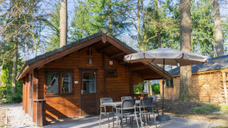 Foto van Stuga 4 lodge, een knusse houten blokhut met terras, tuinmeubilair en parasol in het bos.
