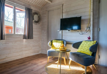 Sala luminosa con dos sillas modernas, cojines amarillos, TV en la pared y ventana en Stuga 4, De Utrechtse Heuvelrug.