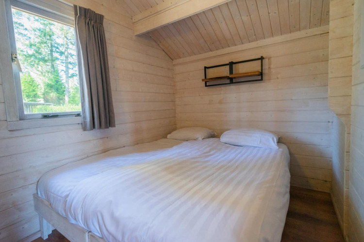 Schlichtes Schlafzimmer in einer Holzhütte mit Doppelbett und Fenster, Stuga 4, De Utrechtse Heuvelrug, Niederlande.