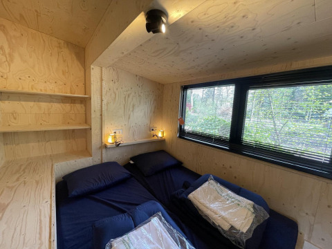 Camera da letto di tiny house moderna con due letti, grandi finestre e pareti in legno chiaro a De Utrechtse Heuvelrug, Paesi Bassi.