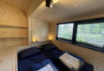 Dormitorio moderno en tiny house con dos camas, grandes ventanas y paredes de madera clara en De Utrechtse Heuvelrug, Países Bajos.