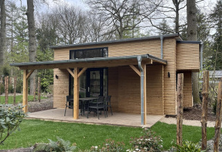 Klein houten huisje met overdekt terras en tuinmeubels bij De Utrechtse Heuvelrug, Nederland.