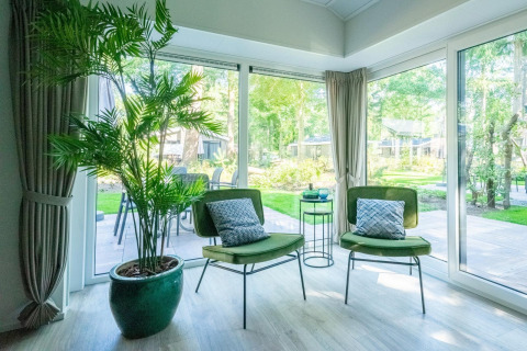 Bright lounge in Velthorst 4 lodge at De Utrechtse Heuvelrug, Netherlands, with green chairs and garden view.