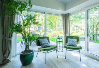 Bright lounge in Velthorst 4 lodge at De Utrechtse Heuvelrug, Netherlands, with green chairs and garden view.