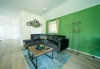 Sala de estar del lodge Velthorst 4 en De Utrechtse Heuvelrug, Países Bajos, con pared verde y sofá gris.