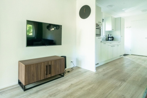 Moderne lodge woonkamer met flatscreen-tv, houten kast en keuken in Velthorst 4, De Utrechtse Heuvelrug.