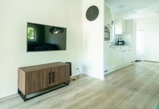 Moderne lodge woonkamer met flatscreen-tv, houten kast en keuken in Velthorst 4, De Utrechtse Heuvelrug.