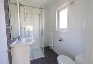 Moderne badkamer met douche, lavabo, toilet en raam in Velthorst 4, De Utrechtse Heuvelrug, Nederland.