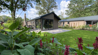 Velthorst 6 lodge with large windows, modern terrace, green garden, flowers, and trees on a sunny day.