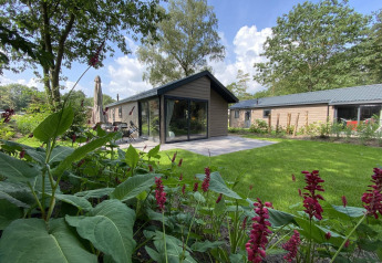Lodge Velthorst 6 met grote ramen, terras en een groene tuin, omringd door bloemen en bomen.