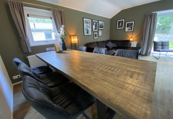 Sala en la cabaña Velthorst 6 en De Utrechtse Heuvelrug, Países Bajos, con mesa de madera y sofás.