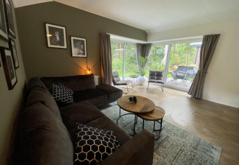 Woonkamer in Velthorst 6 aan De Utrechtse Heuvelrug, Nederland, met zetel, tafels en grote ramen.