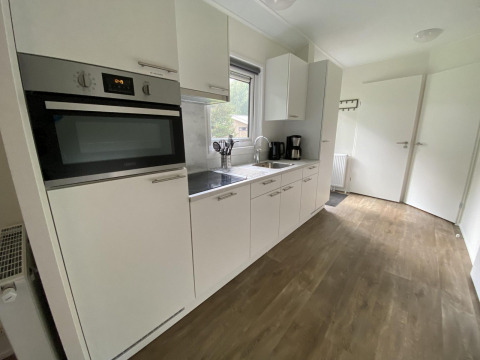 Cocina moderna en la cabaña Velthorst 6 de De Utrechtse Heuvelrug, Países Bajos, con muebles blancos y suelo de madera.