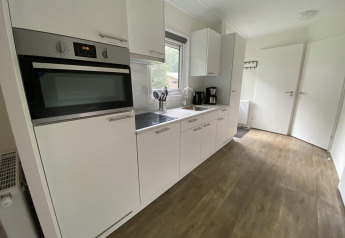 Cocina moderna en la cabaña Velthorst 6 de De Utrechtse Heuvelrug, Países Bajos, con muebles blancos y suelo de madera.