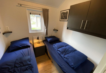Kleine kamer met twee eenpersoonsbedden, donkerblauw beddengoed en raam in Velthorst 6, Nederland.