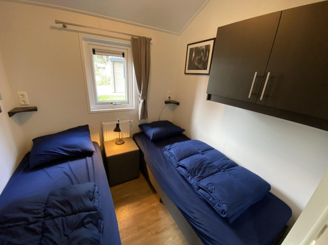 Kleines Zimmer mit zwei Einzelbetten, dunkelblauer Bettwäsche, Fenster und Schrank in Velthorst 6, Niederlande.