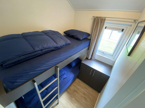 Habitación pequeña con literas, ropa de cama azul, ventana y armario en Velthorst 6, De Utrechtse Heuvelrug, Países Bajos.