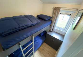 Kleine kamer met stapelbed, blauwe lakens, raam en kast in Velthorst 6, De Utrechtse Heuvelrug, Nederland.