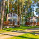 To Air Lodge hytter i en solrig skov med træterrasser, omgivet af høje fyrretræer og grøn græsplæne.