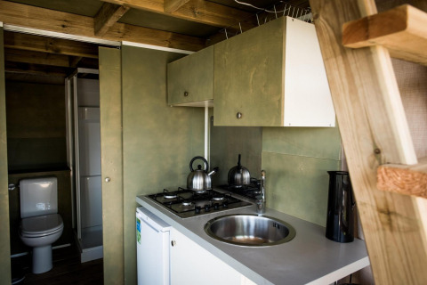 Kleine keuken en badkamer in Air Lodge, Hoge Kempen, België, met fornuis, gootsteen, waterkoker en houtinterieur.