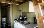 Compacte keuken en badkamer in Air Lodge, Hoge Kempen, België, met fornuis, gootsteen, waterkoker en hout.