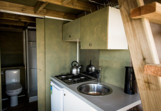 Pequeña cocina y baño en Air Lodge, Hoge Kempen, Bélgica, con cocina, fregadero, tetera e interior de madera.
