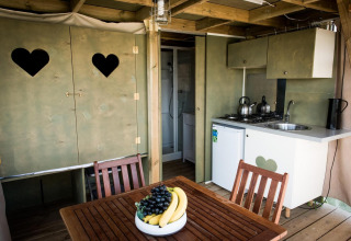 Interiør af Air Lodge på Hoge Kempen i Belgien med et lille køkken, spisebord og skab med hjerteformede vinduer.