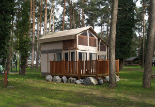 Foto van de Air Lodge bij Hoge Kempen in België, omringd door hoge bomen en een grasveld.