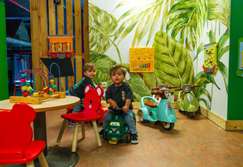 Dos niños pequeños juegan en una sala de juegos colorida de un lodge, con juguetes y scooters decorativos.