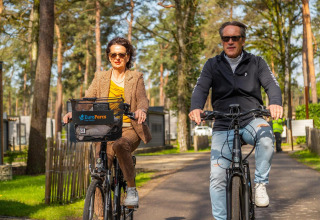 Dos adultos montan bicicletas en un alojamiento de glamping rodeado de árboles, ambos con gafas de sol.