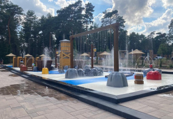 Waterpark bij een lodge, omringd door bomen en parasols, met fonteinen en speelse installaties.