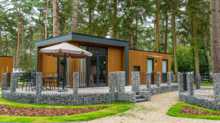 Cabina glamping nella foresta con pannelli in legno moderno, terrazza arredata e recinzione in pietra.
