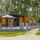 Glamping-cabin i en skov med moderne træbeklædning, terrasse, møbler og stenhegn omkring.