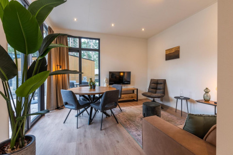 Salon de glamping moderne avec grandes fenêtres, table à manger, plante verte et mobilier confortable.