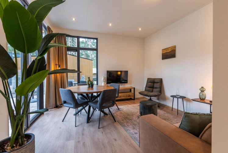 Sala de glamping moderna con grandes ventanales, mesa de comedor, planta verde y muebles cómodos.