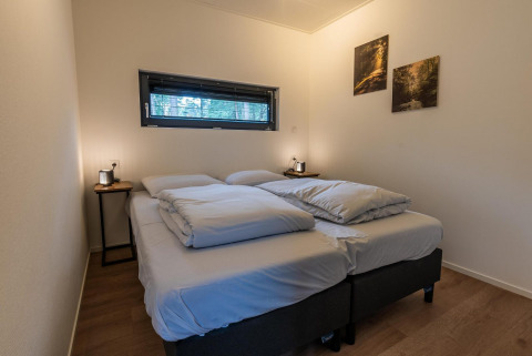 Chambre de glamping moderne avec deux lits, tables de chevet, photos de nature et grande fenêtre.