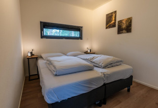 Chambre de glamping moderne avec deux lits, tables de chevet, photos de nature et grande fenêtre.