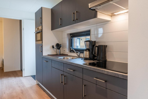Cocina moderna de glamping con armarios grises, cafetera, hervidor eléctrico y horno en ambiente luminoso.