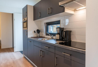 Cocina moderna de glamping con armarios grises, cafetera, hervidor eléctrico y horno en ambiente luminoso.
