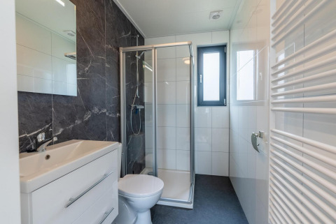 Moderne badeværelse med bruser, toilet og vask i glampingindkvartering med store vinduer og fliser.