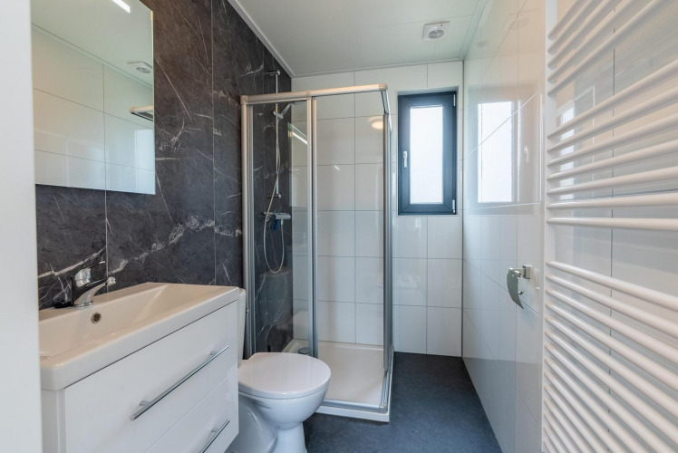 Baño moderno con ducha, inodoro y lavabo en alojamiento glamping, decorado con azulejos blancos y ventana.