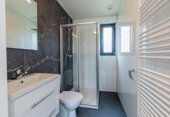Salle de bains moderne avec douche, WC et lavabo dans un hébergement glamping, carrelée et lumineuse.