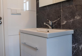 Lavabo moderno con mobile bianco e parete effetto marmo nel Baby Cottage a Hoge Kempen, Belgio.