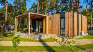 Moderne træhytte med terrasse og grønne stole i skovområde, ideel til afslappende udendørs ophold.